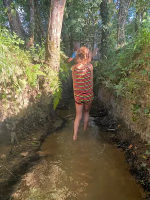 Enfant marchant pieds nus dans l’eau d’un ruisseau sur le sentier pieds nus du Domaine de Larrous – Domaine de Larrous, Gaujacq (Landes)