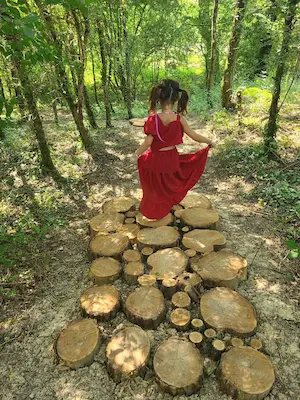 Enfant marchant pieds nus sur des rondins de bois en forêt sur le sentier pieds nus du Domaine de Larrous – Domaine de Larrous, Gaujacq (Landes)