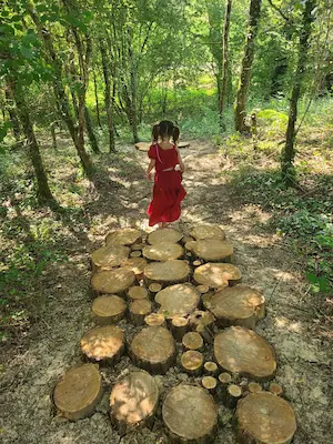 Enfant marchant sur des rondins de bois en forêt sur le sentier pieds nus du Domaine de Larrous – Domaine de Larrous, Gaujacq (Landes)